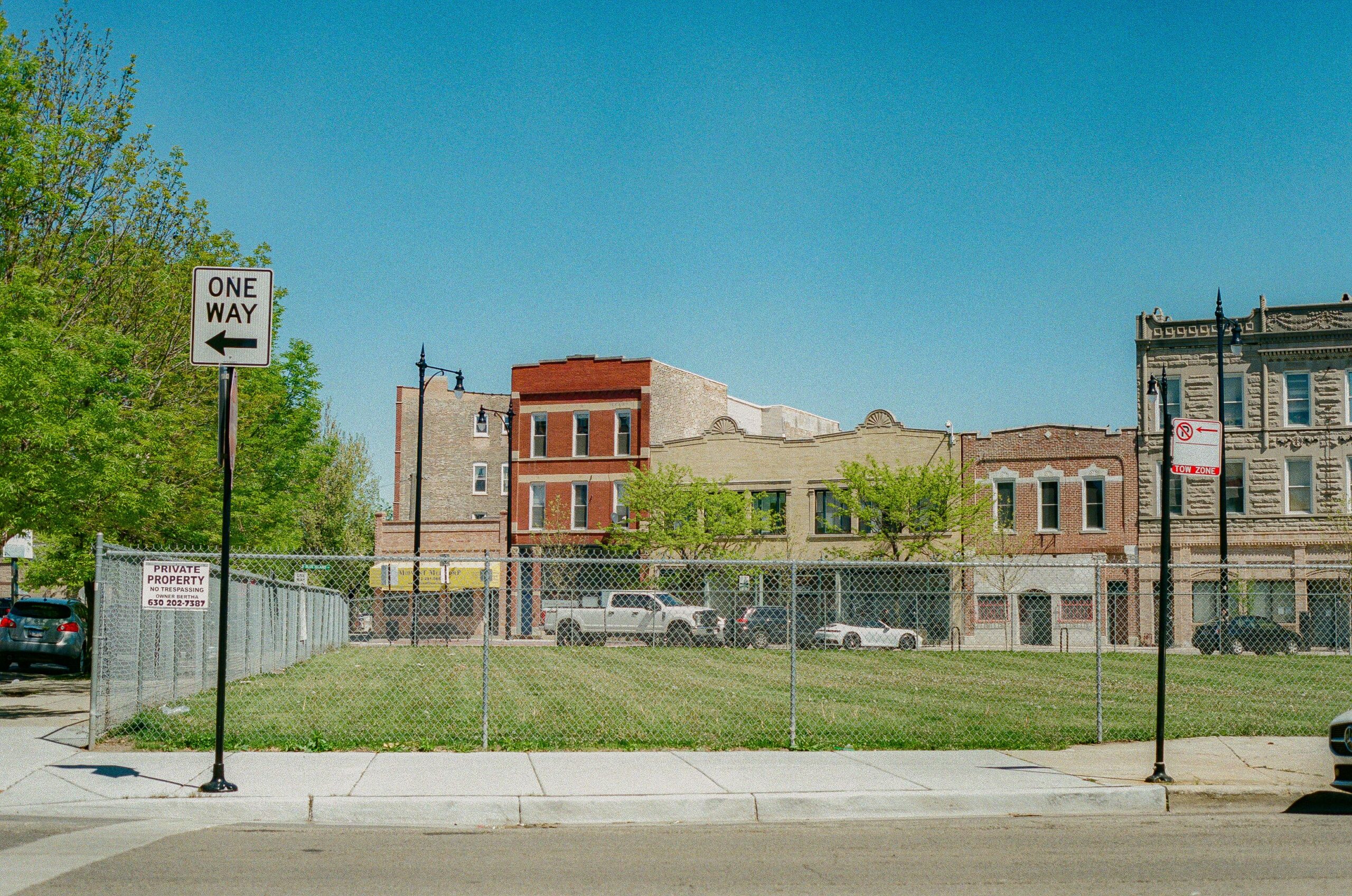 A street view in Chicago showing a vacant lot with surrounding buildings and clear blue sky